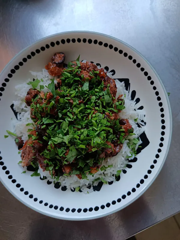 Das Bild zeigt einen weißen Teller, gefüllt mit einer köstlichen Mahlzeit aus Reis, Fleisch und Gemüse. Der Teller ist gedeckt.