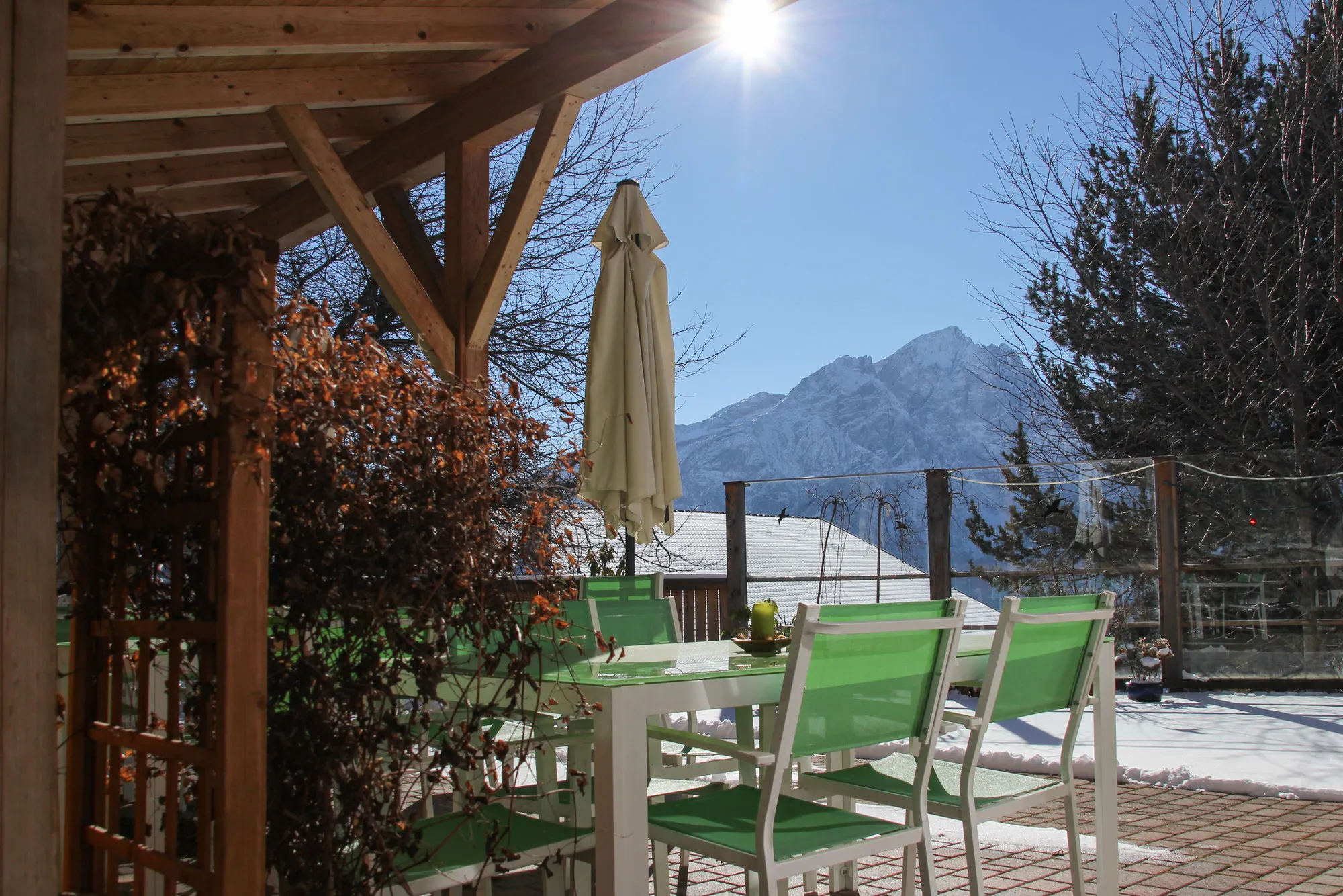 Das Bild zeigt einen Terrassentisch mit grünen Stühlen, umgeben von einer wunderschönen Aussicht auf schneebedeckte Berge. Der Tisch ist gedeckt.